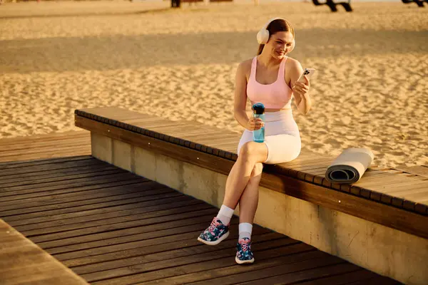Una joven comprueba felizmente sus estadísticas de fitness en la costa arenosa. - foto de stock