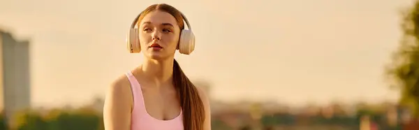 Focused young woman wears headphones as she prepares for her workout in a vibrant outdoor setting — Stock Photo