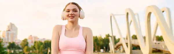 A fit young woman in athletic gear smiles while exercising outdoors by a city bridge. — Stock Photo