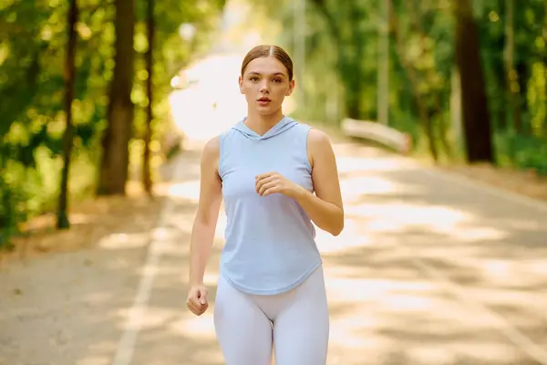 A young woman jogs energetically on a serene forest trail in a lush green setting. — Stock Photo