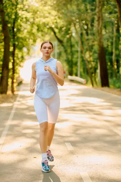 Una giovane donna corre su un sentiero alberato, godendo il suo allenamento sotto la calda luce del sole. — Foto stock