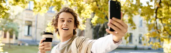 A handsome student captures a joyful moment outdoors, smiling and holding a coffee cup. — Stock Photo