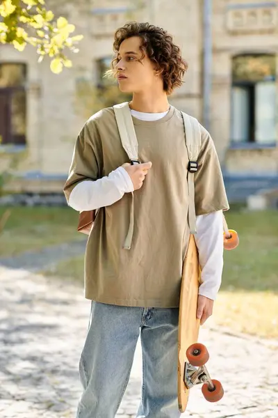 A young man stands outside on a lovely day, skateboard in hand, pondering life. — Stock Photo