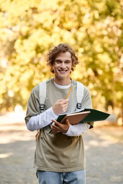 A stylish young man studies outdoors, smiling with books and a pencil in hand. — Stock Photo
