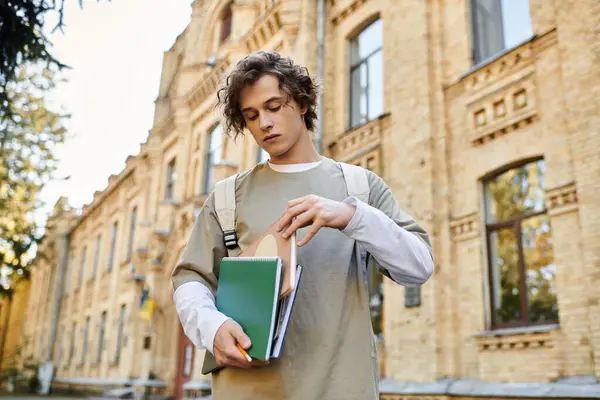Handsome student holding study materials while preparing to enter a charming university. — Stock Photo