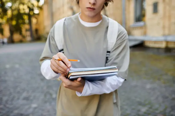 Handsome student engaged in writing with a pencil in a vibrant outdoor environment — Stock Photo