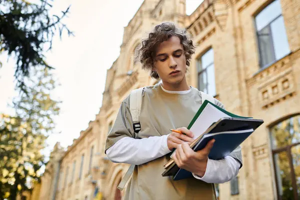 Jovem confiante vestido em estilo casual mantém cadernos e escreve enquanto estuda ao ar livre. — Fotografia de Stock
