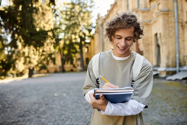 Estudiante guapo esboza ideas mientras está parado fuera de un edificio histórico a la luz del día. - foto de stock