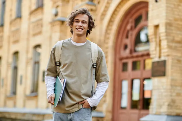 A cheerful student holds notebooks and a pen outside a historic building. — Stock Photo
