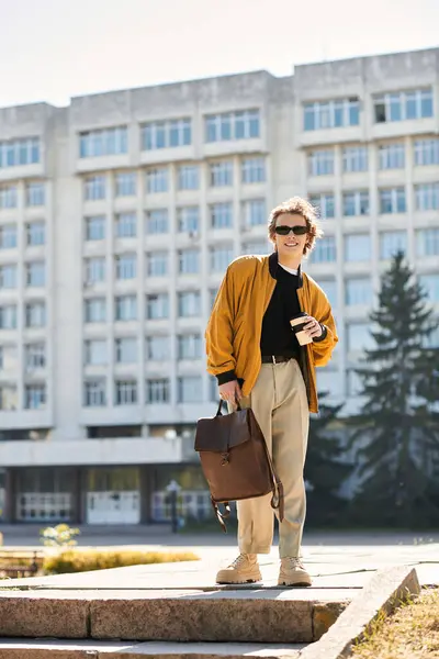 Charming young student poses confidently on campus steps, soaking up the sun while holding coffee. — Stock Photo