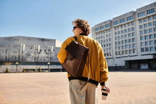 A fashionable young man strolls through an urban area, enjoying his coffee and the bright sunshine. — Stock Photo