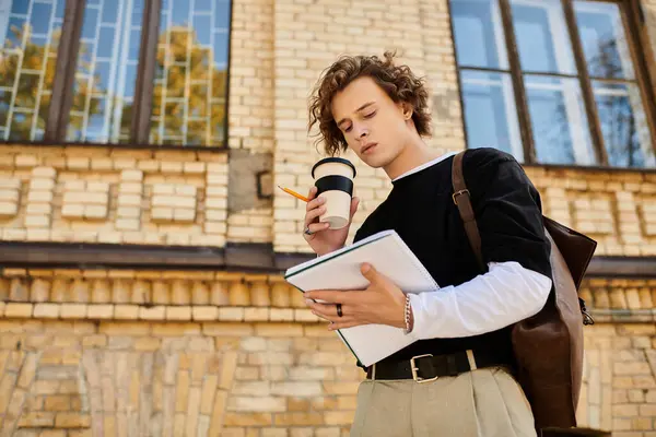 Handsome student enjoys coffee while focused on notebook outside a charming brick structure — Stock Photo