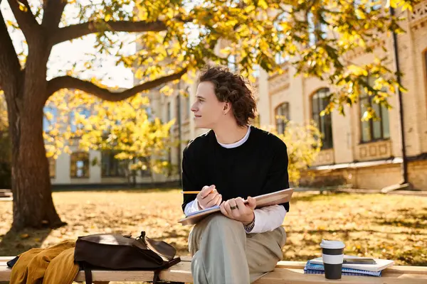 In a vibrant urban park, a young stylish man relaxes on a bench, sketching natures beauty. — Stock Photo