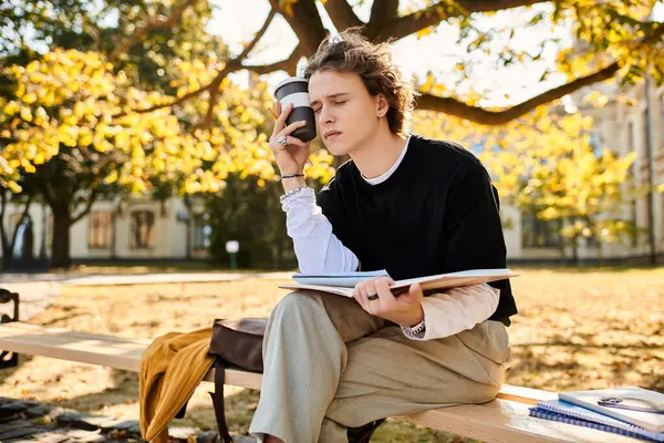 A fashionable young man sits on a bench, sipping coffee and reading notes in a vibrant park. — Stock Photo