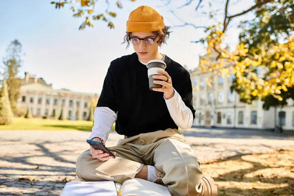 Stylish young man sips coffee and checks his phone while sitting on a sunny park bench — Stock Photo