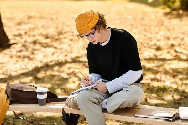 Young man sketches ideas on a notepad while sitting casually in a vibrant autumn park. — Stock Photo