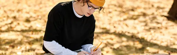 A fashionable young man sits on a bench in a park, focused on writing notes with a pencil. — Stock Photo