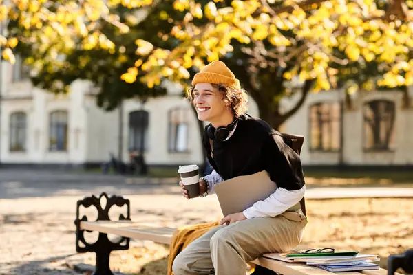 A young man in stylish clothes relaxes on a bench with coffee, studying outdoors. — Stock Photo
