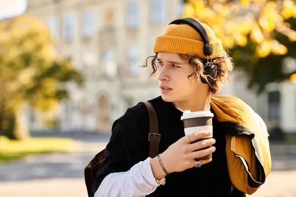A stylish man with headphones sips coffee outside on a sunny day. — Stock Photo