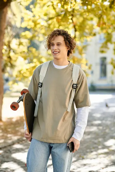 A handsome young student radiates joy while holding a skateboard, surrounded by vibrant trees. — Stock Photo