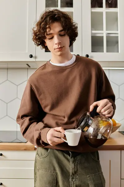 Un joven vierte café en una taza en su elegante apartamento mientras disfruta de una mañana acogedora. - foto de stock