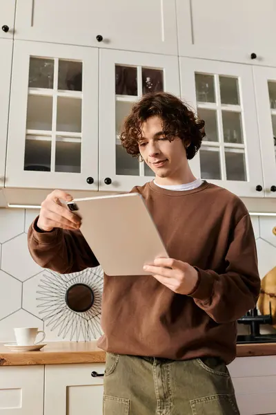 Un joven con una sudadera marrón está usando una tableta en su elegante apartamento. - foto de stock