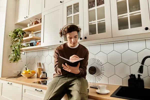 Curly-haired student enjoys writing in a cozy modern apartment kitchen while relaxing. — Stock Photo