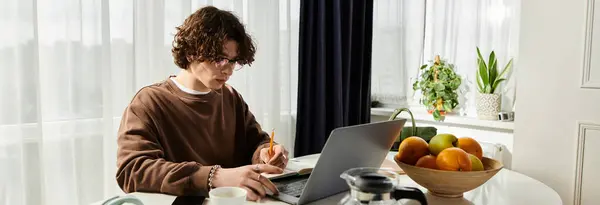 A young man in a brown sweatshirt studies at a sleek table in natural light, banner — Stock Photo