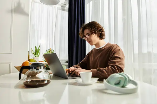 Young man in a brown sweatshirt focuses on his laptop in a bright and modern living space. — Stock Photo