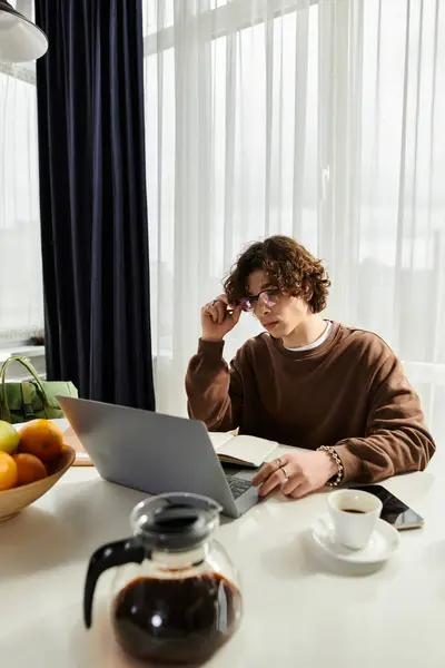 A young man in a brown sweatshirt focuses on his laptop amidst a cozy apartment setting. — Stock Photo