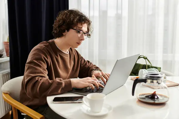 Curly-haired student in brown sweatshirt works intently on his laptop at home. — Stock Photo