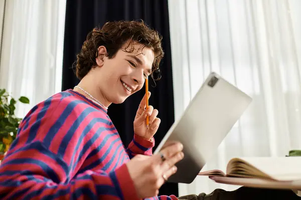 A young non-binary person smiles while studying in a vibrant striped sweatshirt at home. — Stock Photo