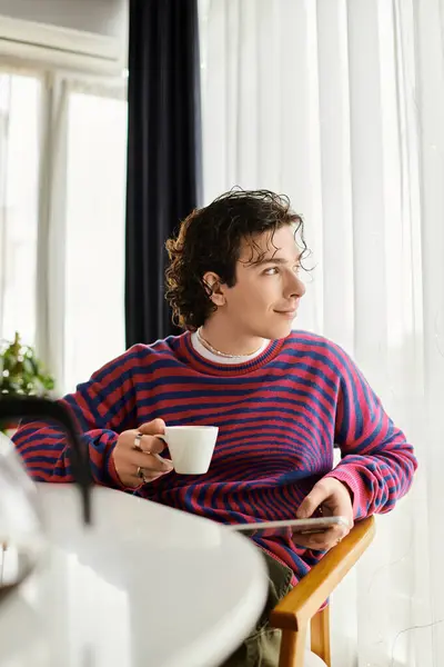 A young person with curly hair relaxes in their stylish apartment, sipping a warm beverage — Stock Photo