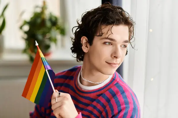 Une jeune personne non binaire sourit tout en tenant un drapeau de fierté dans un appartement dynamique. — Photo de stock