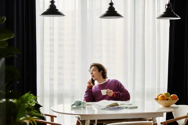 Brightly dressed individual sips tea while engaging in a phone conversation at home. — Stock Photo