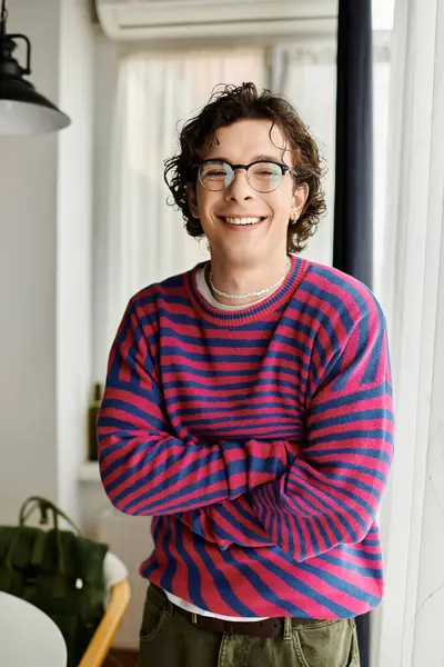 Curly-haired non binary individual radiates happiness in a colorful striped sweatshirt at home. — Stock Photo