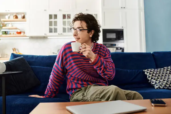 A young non binary person enjoys a warm drink in a vibrant striped sweatshirt at home. — Stock Photo
