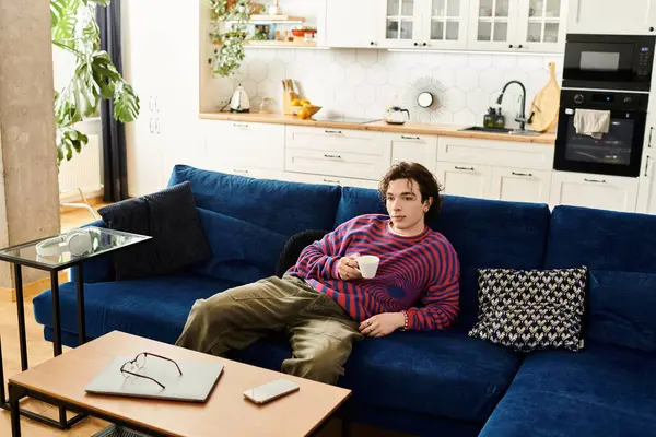 Dans un sweat rayé vibrant, une jeune personne non binaire aime le café tout en se prélassant à la maison. — Photo de stock