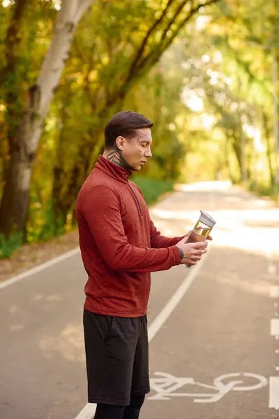 Handsome young man shows off his tattoos while savoring a refreshing drink outdoors in the park. — Stock Photo