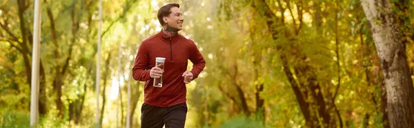 Handsome man with tattoos runs through a colorful park surrounded by golden leaves and trees. — Stock Photo