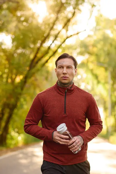 Un hombre guapo y tatuado recorre un tranquilo sendero rodeado de árboles y dorada luz del sol.. - foto de stock