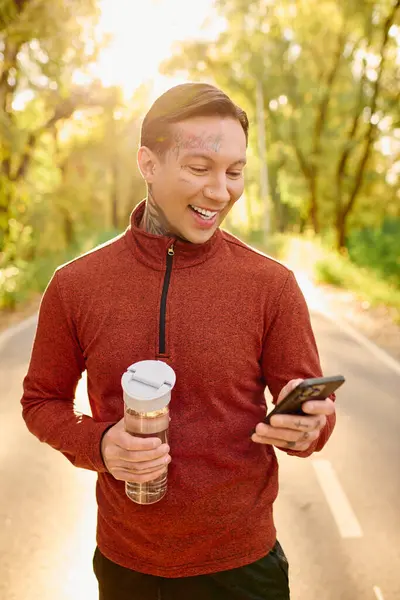 A young man with tattoos smiles brightly while engaging with his smartphone on a vibrant trail. — Stock Photo
