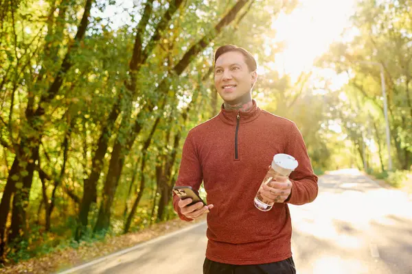 Handsome man in trendy attire takes a leisurely stroll through a sunlit forest path, smiling. — Stock Photo