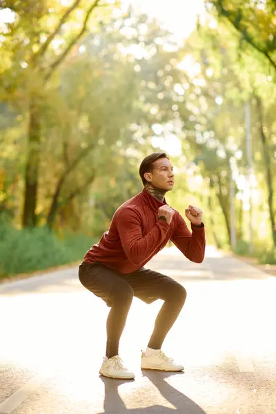 Hombre tatuado hace sentadillas con estilo en un camino de la naturaleza pacífica. - foto de stock