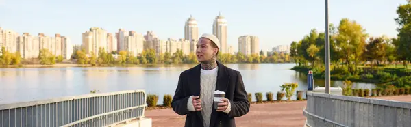 Красавчик, одетый в шикарный костюм, уверенно прогуливается по набережной, наслаждаясь кофе.. — стоковое фото