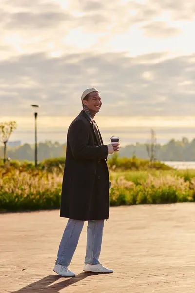 Confident man holding coffee, modeling modern fashion in a peaceful setting. — Stock Photo