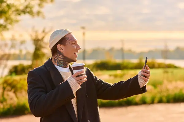 Hombre tatuado sonríe y bebe café, capturando un momento alegre al aire libre. - foto de stock