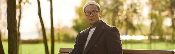 Handsome man donning trendy attire poses on a park bench during a golden hour, exuding coolness. — Stock Photo