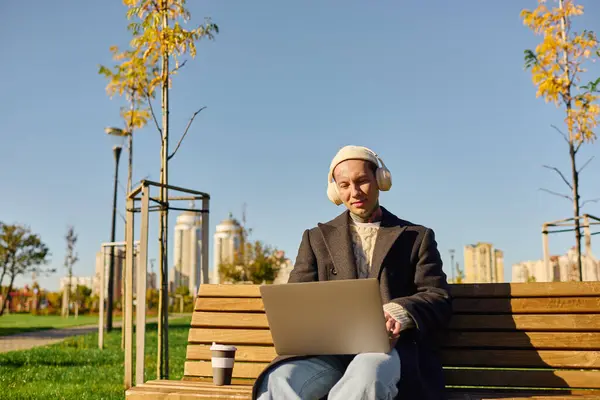 Handsome man with tattoos relaxes on a bench while working on his laptop in the park. — Stock Photo