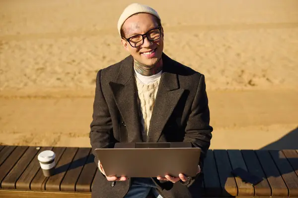 Handsome man with tattoos enjoys working on his laptop while relaxing on a sunny beach. — Stock Photo